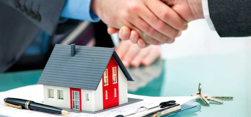 Two people shaking hands over a document, a model home, and house keys.