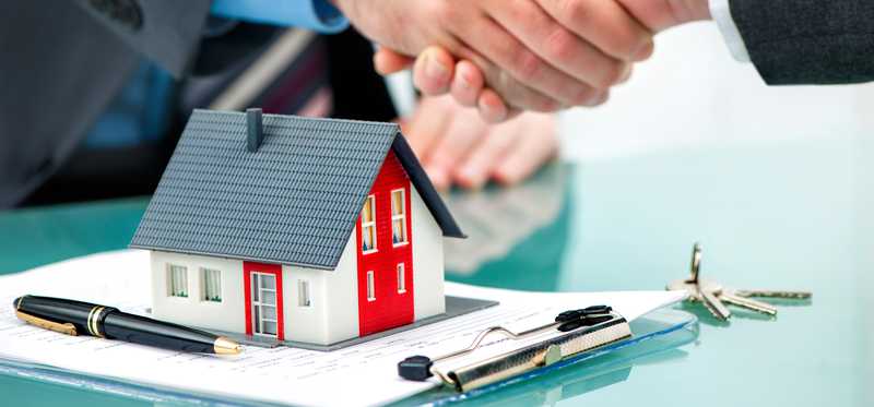 two people shaking hands over a document and a model home