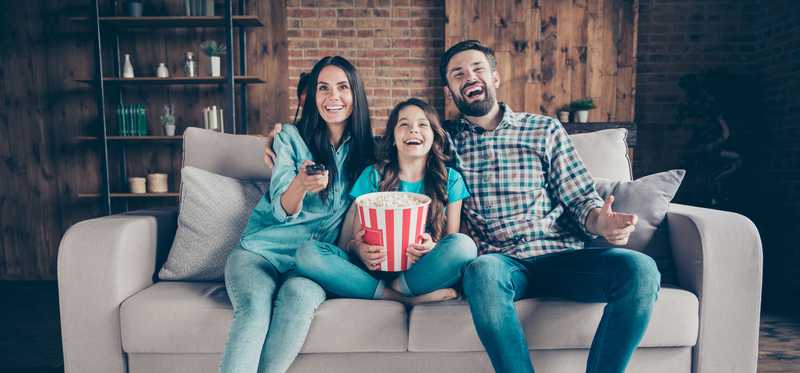 Happy family on couch eating popcorn while watching TV.