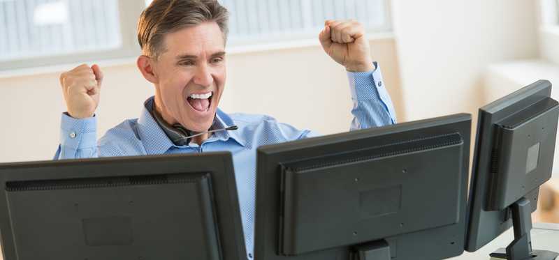 Man raises arms in success in front of computers