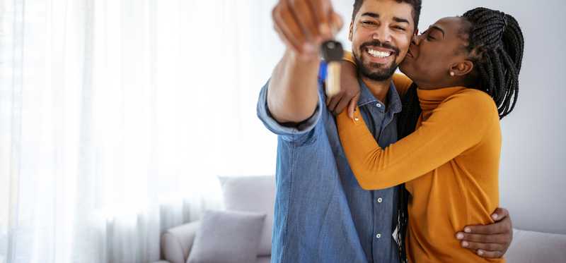Two people smiling and hugging while holding out keys.