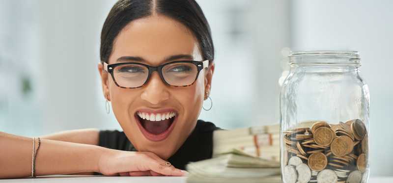 Happy woman in glasses looking at jar of coins