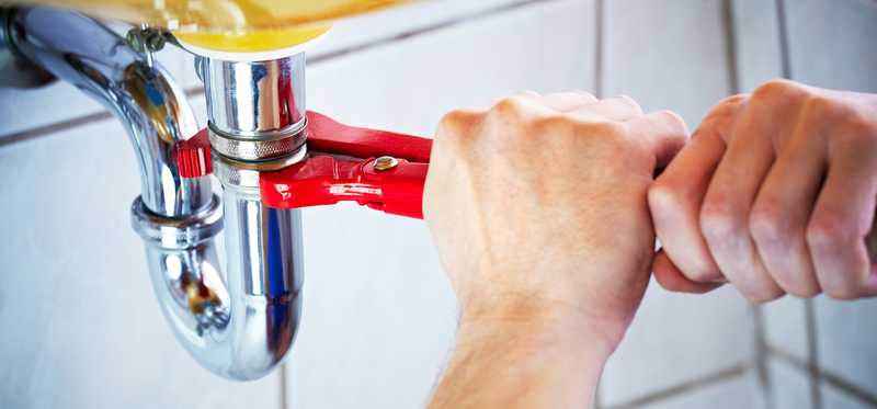 A person repairing a pipe under a sink.
