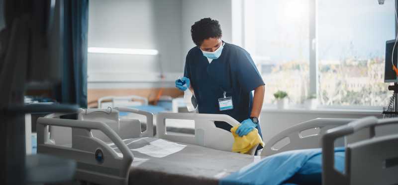 A person in scrubs preparing a hospital bed.