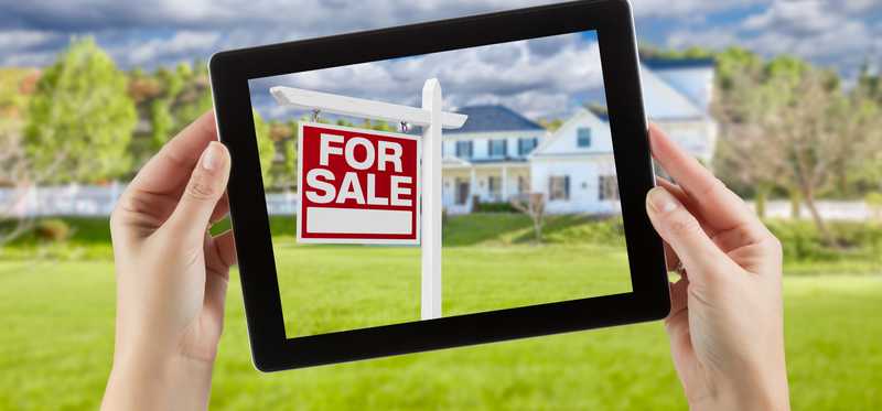 House For Sale sign seen through frame of a tablet.