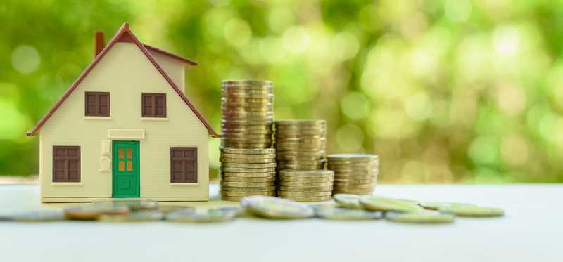 Model of a house next to stacks of coins