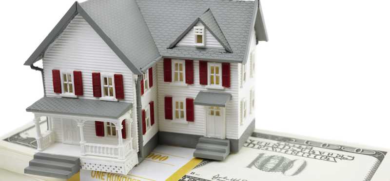 A model of a house sits atop bundles of U.S. $100 bills.