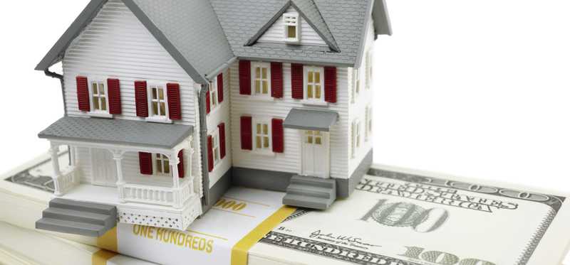 A model of a house sitting atop bundles of $100 bills.