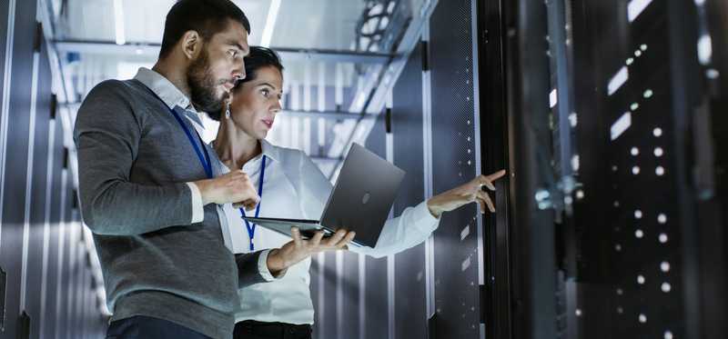 Two workers inspect large pieces of computer equipment.