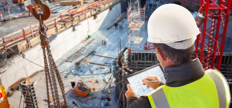 A person wearing a hard hat looking down into a building construction site.