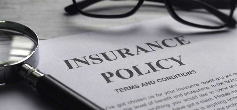 A pair of glasses and a magnifying glass atop a document that says Insurance Policy.