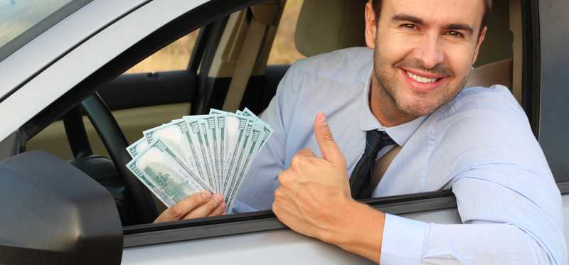 Driver leaning out of a car window holding hundred dollar bills