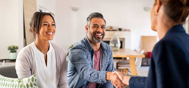 Two people shaking hands with a third person sitting nearby.