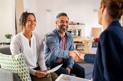 Two people shaking hands with a third person sitting nearby.