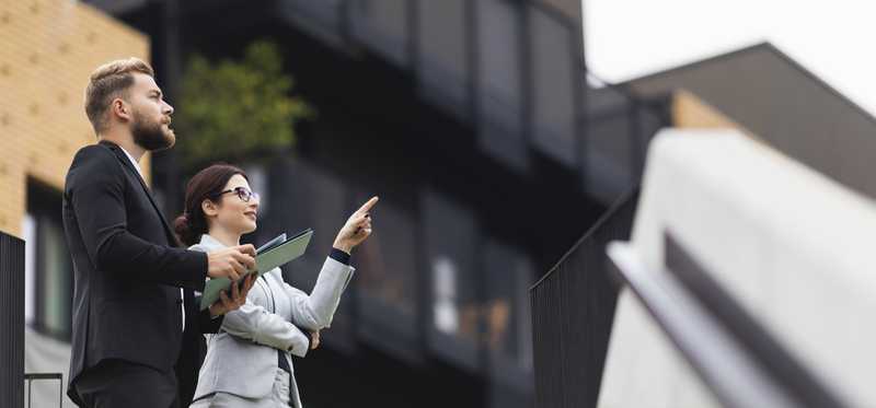 Two professionals point at apartment buildings from the courtyard.