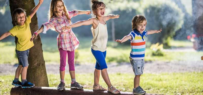 Four kids smile as they balance on elevated log.