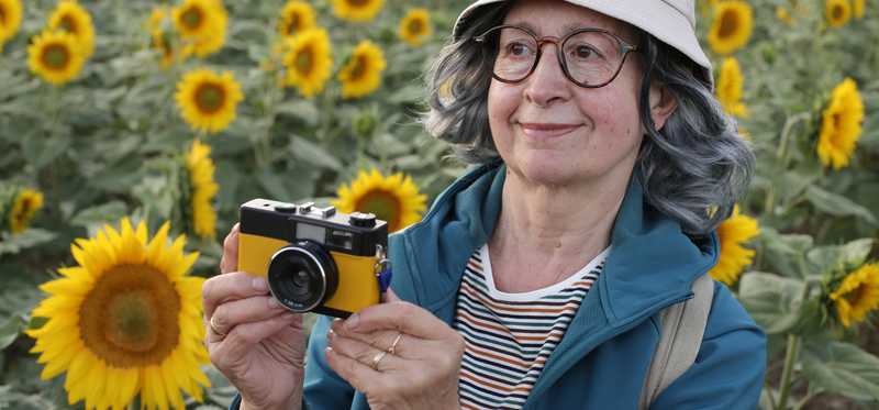 A person standing and holding a camera in a field of sunflowers.