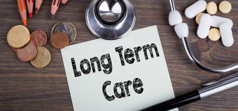 Long term care printed on paper near stethoscope, coins, and medicine.