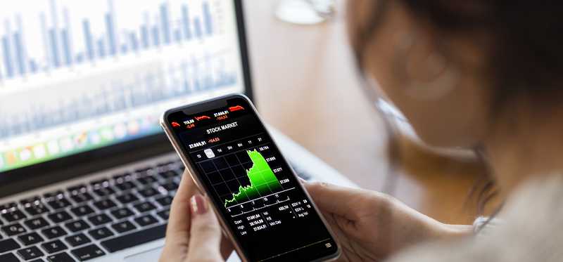 A person looking at stock charts on a computer and phone.