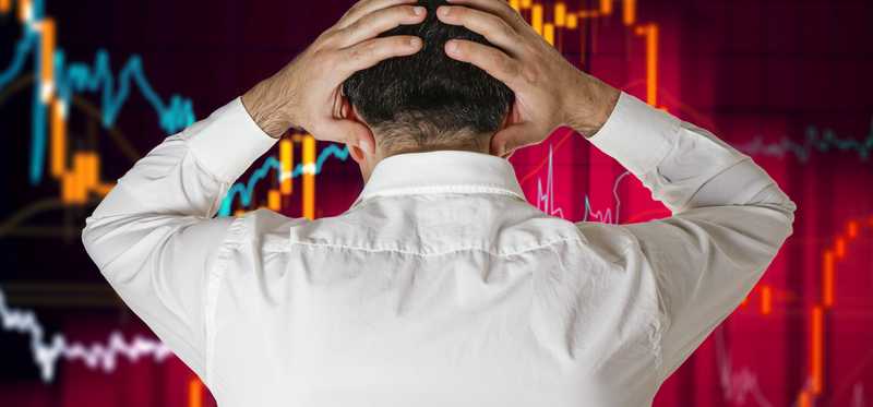 Person holding head and watching stock market crash.