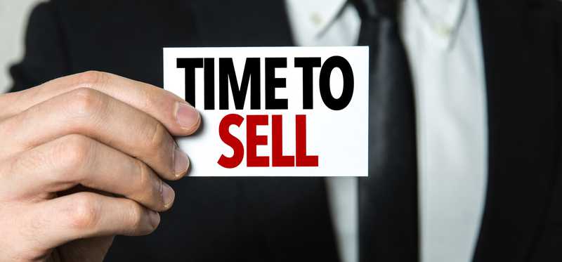 Person in business suit holding sign that says Time to Sell.