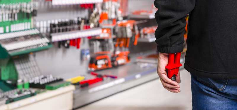 man in hardware store slipping tools up his sleeve