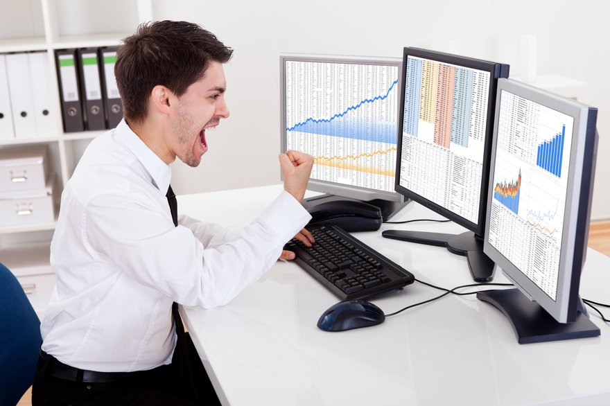 Person in office looking at computer screen with stock chart and celebrating.