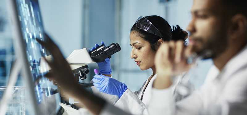 Scientists using a computer and microscope to study life science.