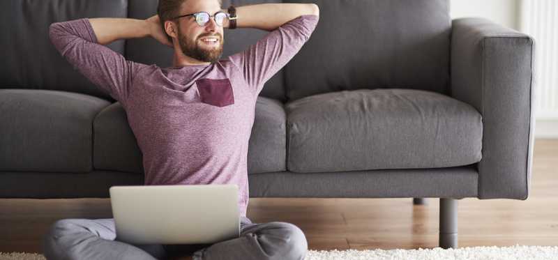 A person relaxes on floor in front of a couch, holding a laptop.