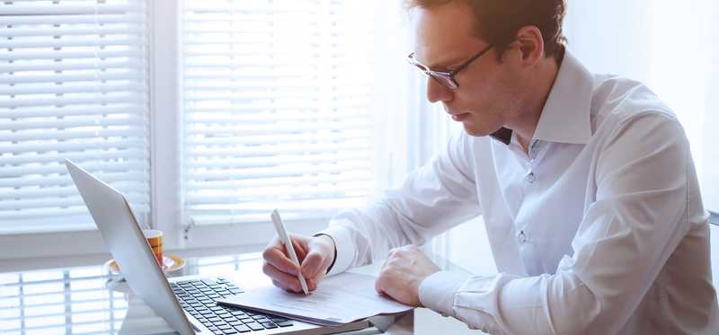 Man reading paper report statement and using laptop