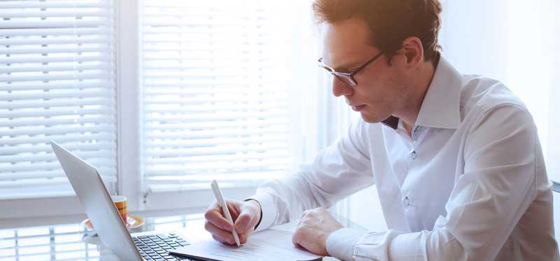 Man reading paper report statement and using laptop.