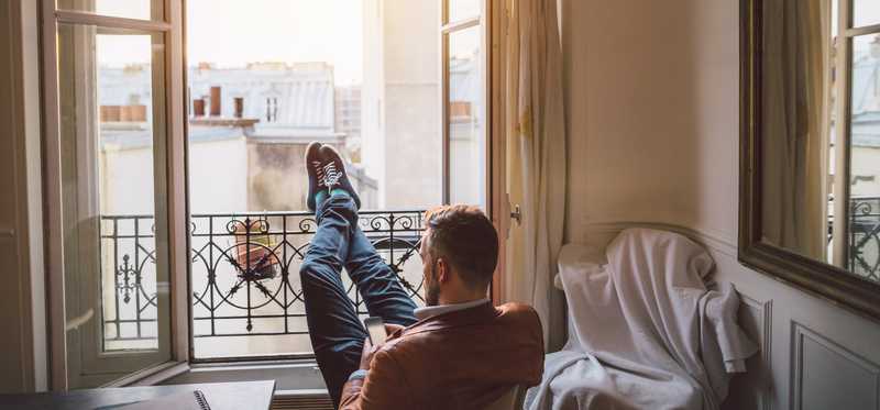 Man looking at phone and sitting with his feet up on open window railing