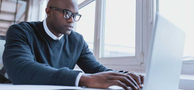 Man in glasses typing on a laptop.