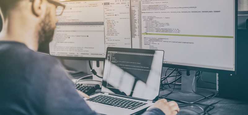Man typing on laptop in front of multiple monitors.
