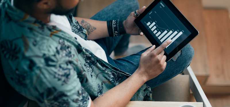 Person uses tablet to view crypto chart while enjoying coffee.