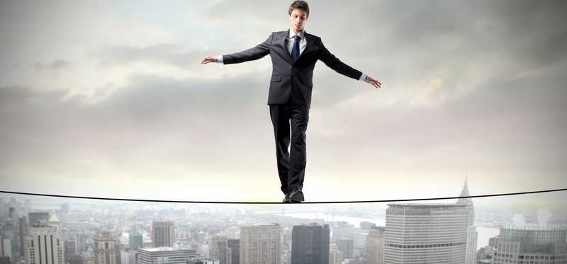 Person in a suit is balancing on a tightrope above a city.