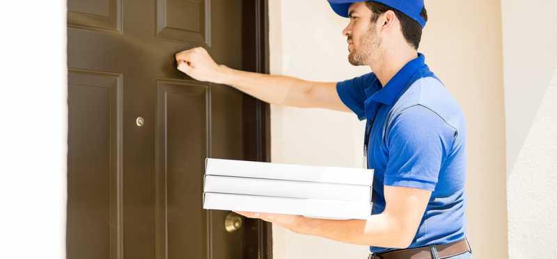 Man in blue uniform with pizza boxes knocking on door.