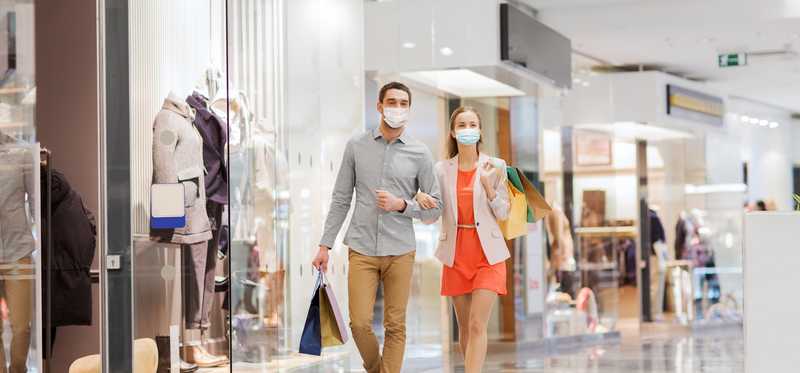 Two people holding shopping bags and walking arm-in-arm through a mall.