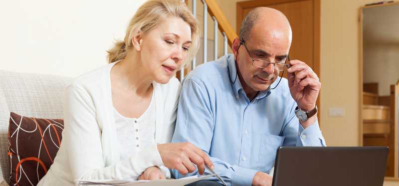 Two people sit on couch with laptop and paperwork.