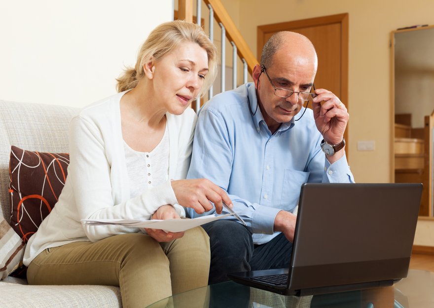 Two people sit on couch with laptop and paperwork.