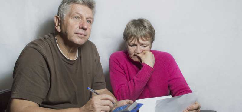 Two worried people sit together with calculator and paperwork.