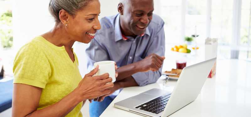Two people sitting in kitchen are looking at laptop computer and smiling.