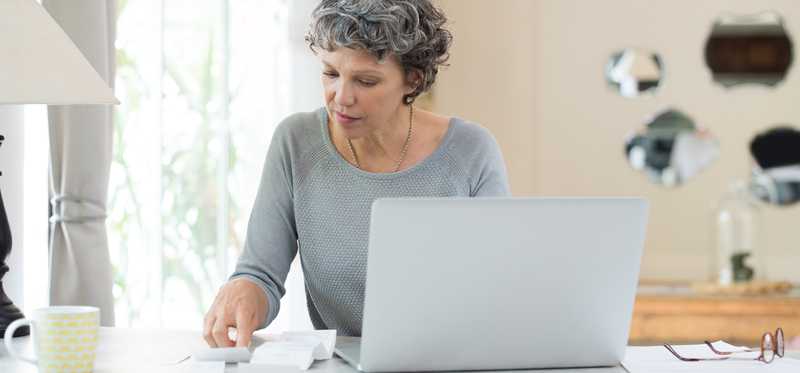 Person sitting at table in front of laptop is looking at receipts.