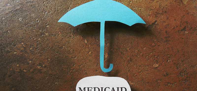 A paper umbrella above a piece of paper with Medicaid written on it.