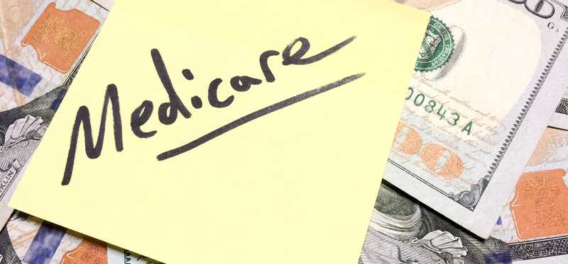 Medicare written on a Post-it note on a pile of hundred dollar bills.