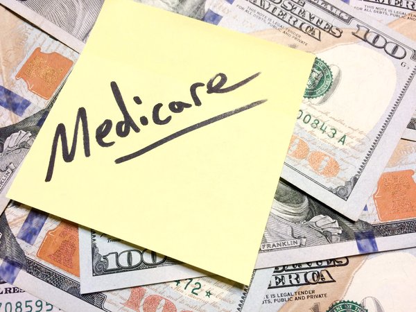 Medicare written on a Post-it note on a pile of hundred dollar bills.