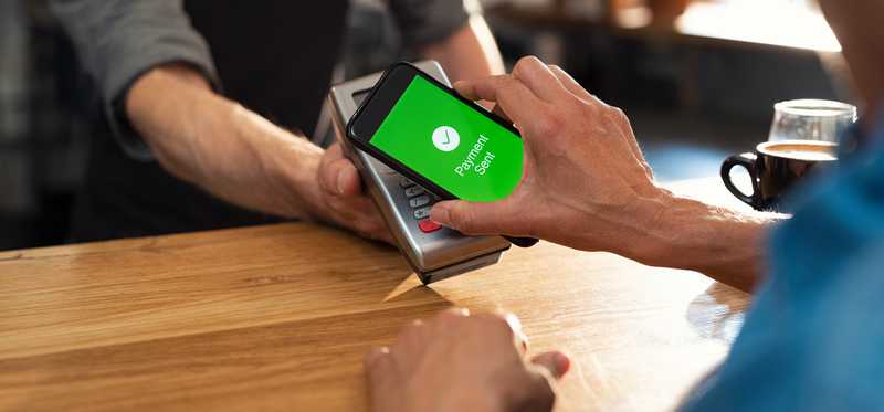 Person holding phone up to reader to buy something using mobile payment processing