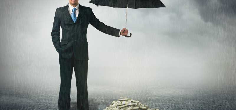Man in suit holding an umbrella over a pile of money