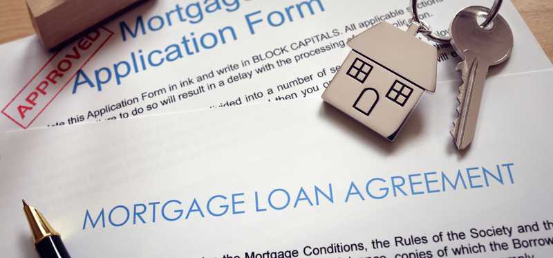 A house key lying on top of a mortgage loan application and agreement forms.