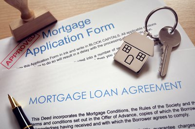 A house key lying on top of a mortgage loan application and agreement forms.